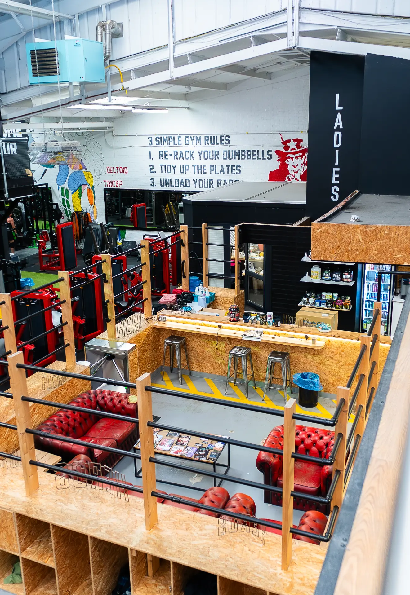 Heros reception, shake bar and red leather lounge below the '3 Simple Gym Rules' mural